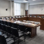 Empty regulatory hearing room with microphones and document exhibits on a long table